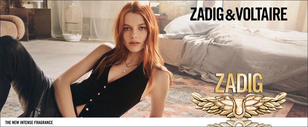 Рекламен банер на Zadig & Voltaire с червенокоса жена и парфюма Zadig в интериор на спалня. В долната част е изписано „The New Intense Fragrance“.